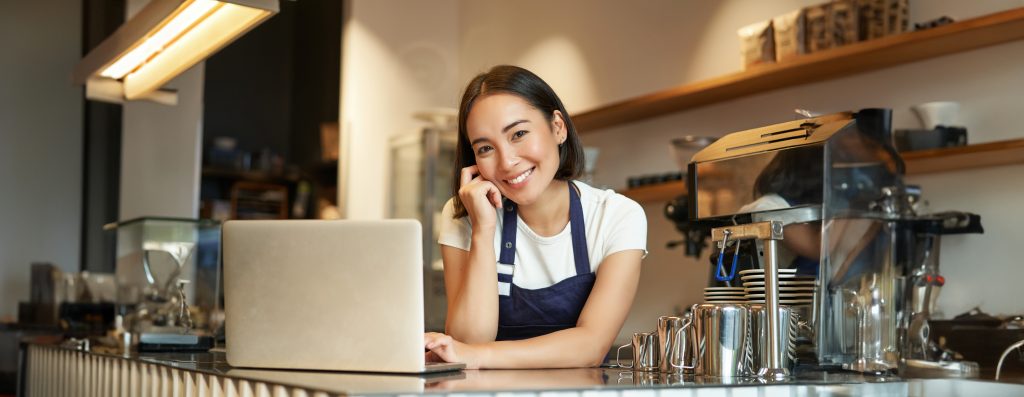 portrait smiling korean woman barista coffee shop standing counter with laptop smiling